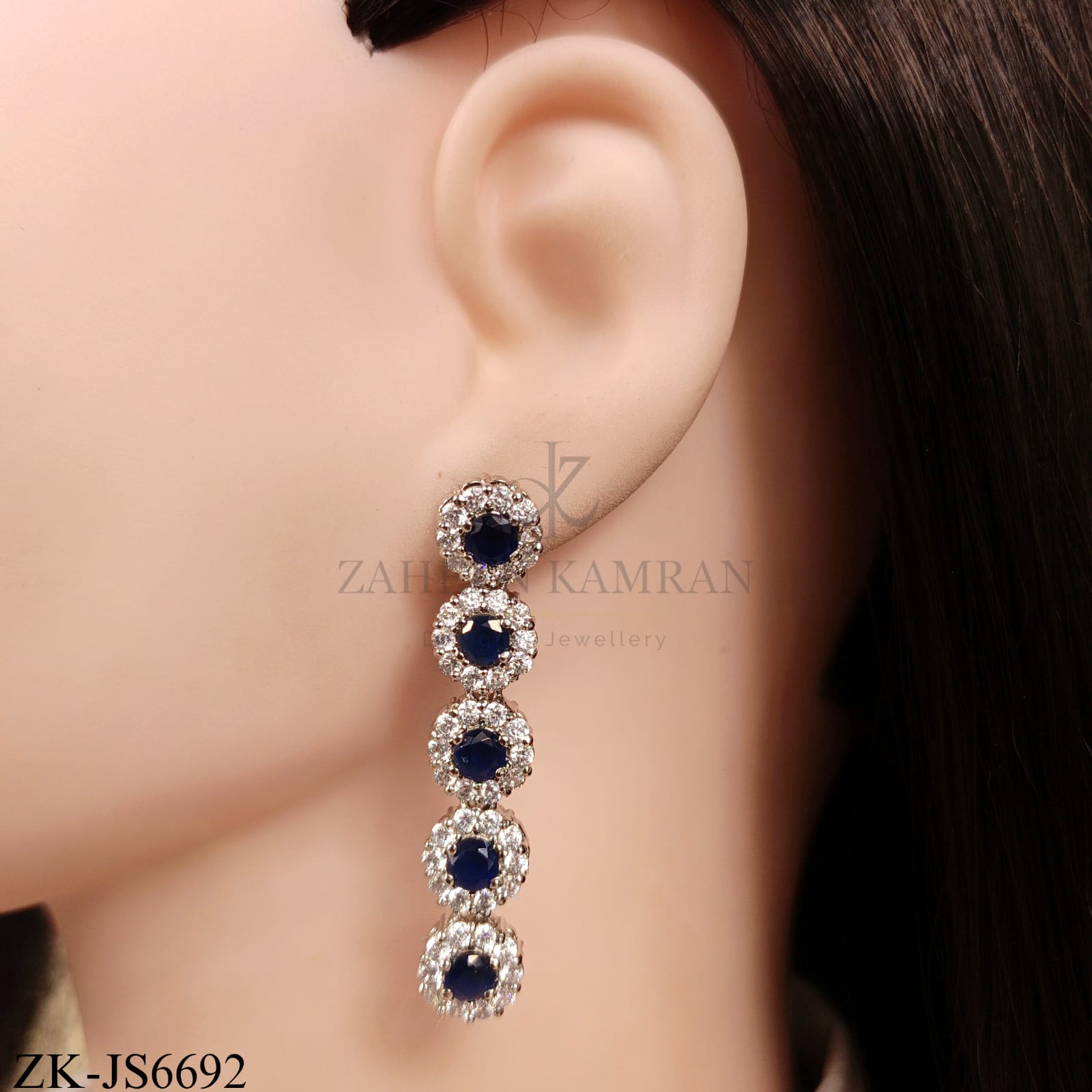 Elegant designer necklace and earring set featuring sparkling sapphire surrounded by zirconia in a silver metal finish.